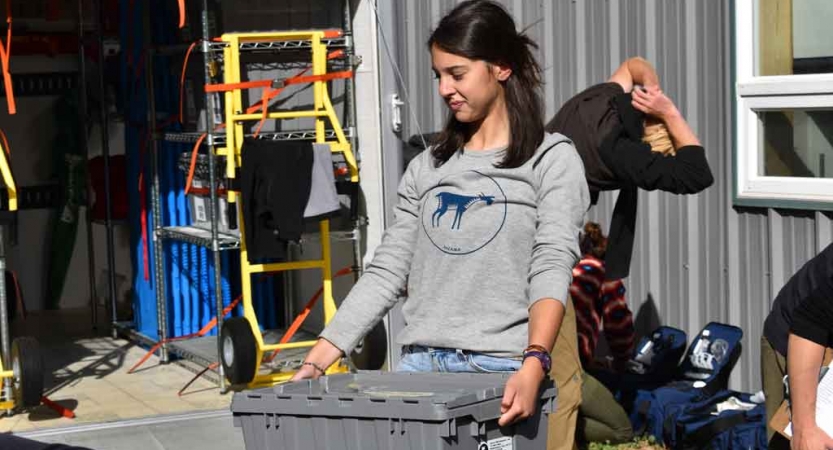 A person carries a plastic crate during a service project with outward bound